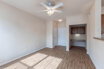 a living room with hardwood floors and a ceiling fan. A built-in desk and overhead storage.